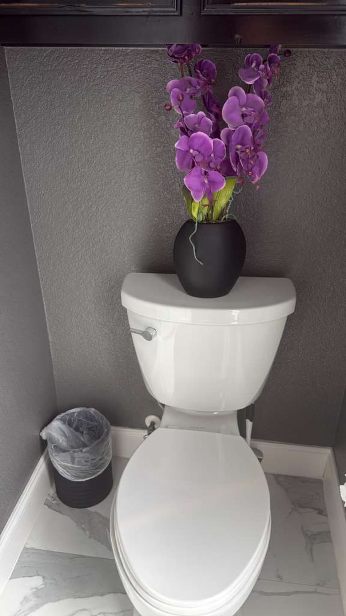 Clean bathroom toilet area with fresh liner and decorative orchid.