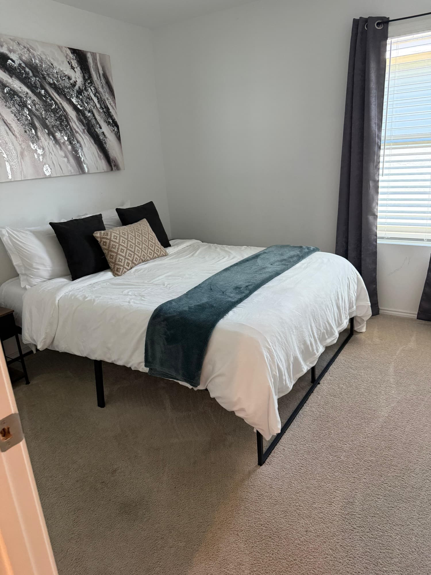 Clean bedroom with white bedding, teal throw, and gray curtains.